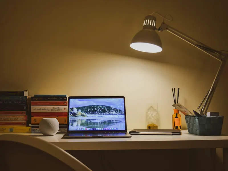 Un ordinateur portable ouvert sur un bureau, éclairé par une lampe le soir