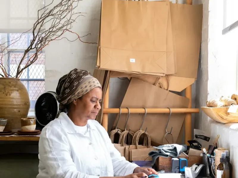 Une commerçante prépare une commande dans sa boutique, entourée de sacs kraft