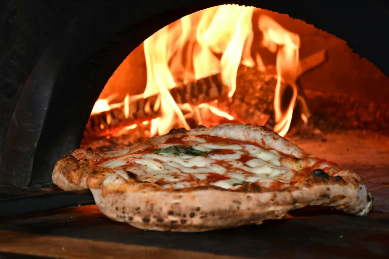 Une pizza margherita en cuisson dans un four à bois